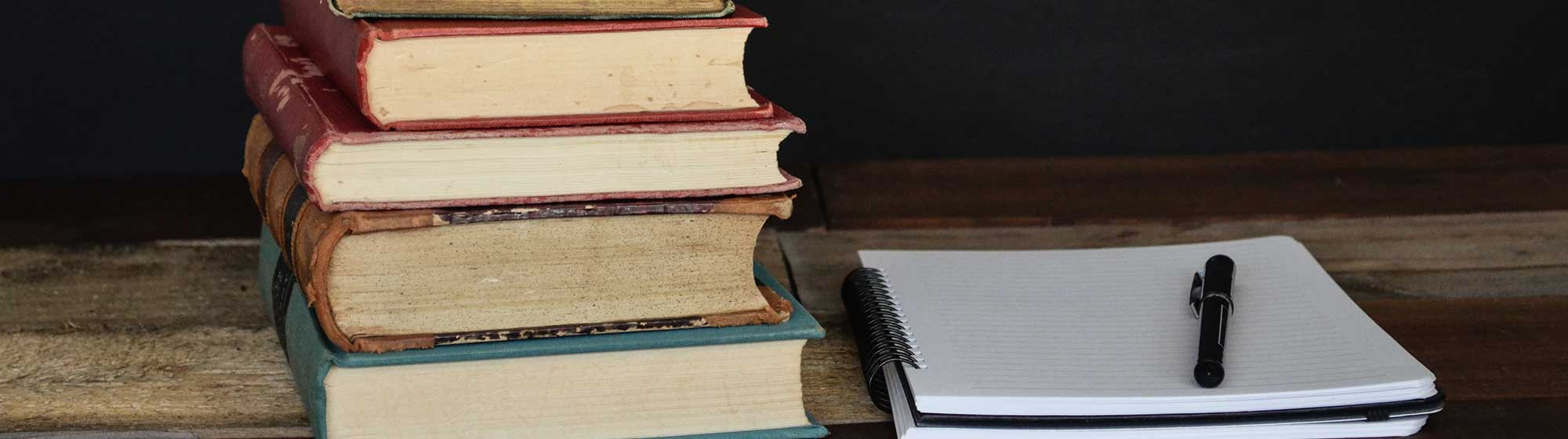 Pile de livres sur un bureau avec un cahier de notes 